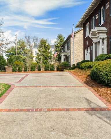Brick driveway with iron gates leading to brick colonial buildings with manicured hedges and landscaping