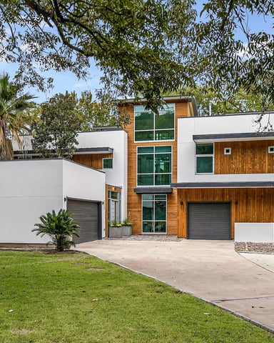 Modern two-story house with white and wood exterior, double garage, surrounded by mature trees and green lawn.