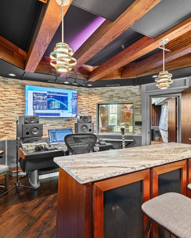 Professional music studio with wooden beams, marble-top island, keyboards, monitors, speakers, and electric guitars on wall