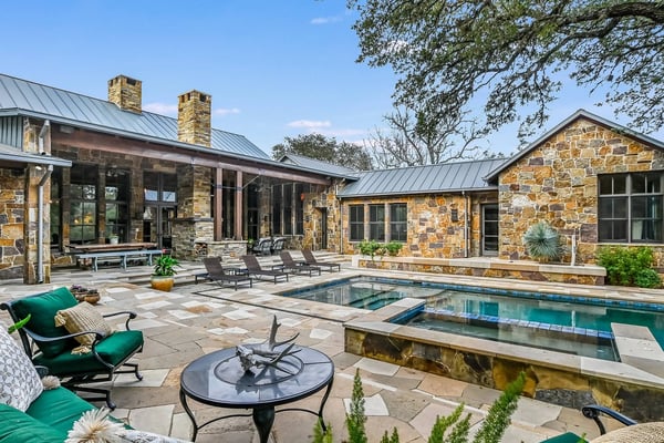 Stone ranch house with metal roof, pool, and patio with lounge chairs and fire pit