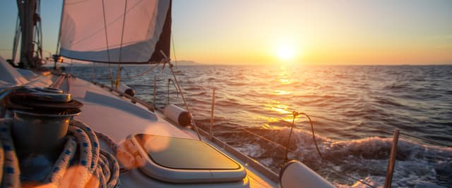 Sailboat deck at sunset with billowed sail, rope, and ocean waves in golden light