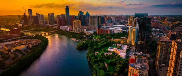 Aerial view of downtown Austin skyline at sunset with Colorado River, green park, and golden-lit buildings