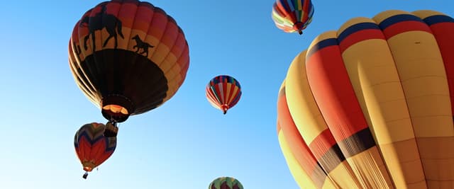 Multiple colorful hot air balloons floating in clear blue sky during daytime