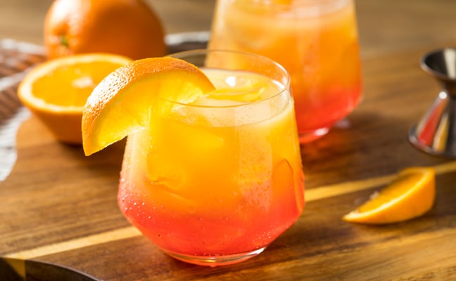 Iced orange cocktails with orange slices and fresh oranges on wooden surface