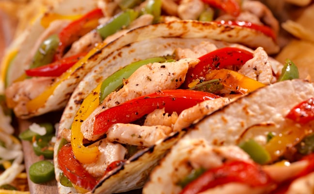 Grilled chicken fajitas with red and yellow peppers and green onions on seeded tortillas